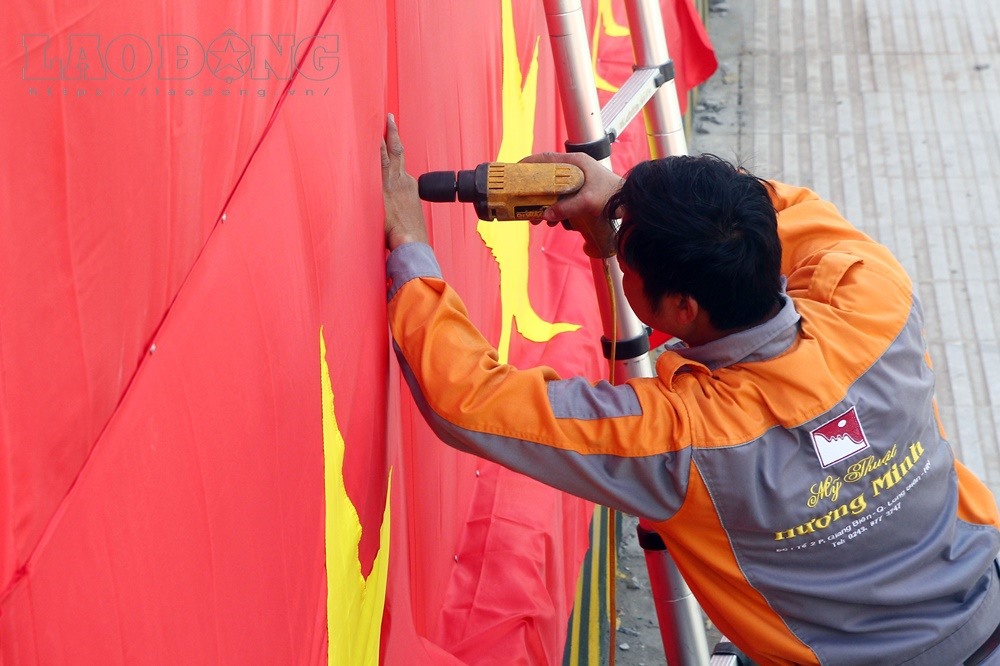 Các công nhân đang gắn những lá cờ Quốc kỳ xung quanh tường rào công trình xây dựng.