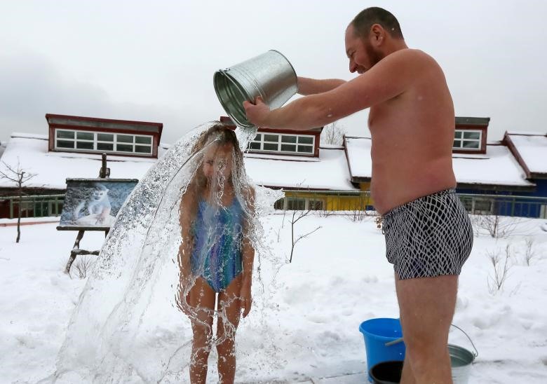 Mặc dù nhiệt độ ngoài trời là 5 độ C nhưng Grigory Broverman - một thành viên câu lạc bộ bơi lội mùa đông, đổ một xô nước lạnh trên con gái Liza 9 tuổi của mình trong buổi lễ Polar Bear Day.  Ảnh: REUTERS.
