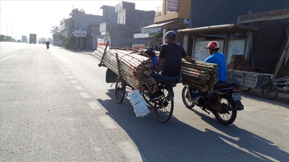 Xe máy đẩy xích lô chở cọc che không được che chắn, nặng nhọc di chuyển trên phố Nguyễn Bỉnh Khiêm. 
