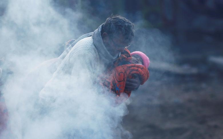 Một người đàn ông bế đứa trẻ quấn trong chăn từ đống lửa vào buổi sáng mùa đông lạnh lẽo ở New Delhi (Ấn Độ). Ảnh: Reuters.