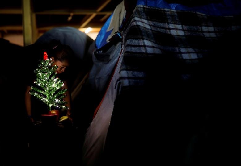 Một người phụ nữ nằm trong đoàn người di cư từ Trung Mỹ đến Hoa Kỳ   đặt một cây thông Giáng sinh trước lều của cô tại nơi trú ẩn tại Tijuana, Mexico