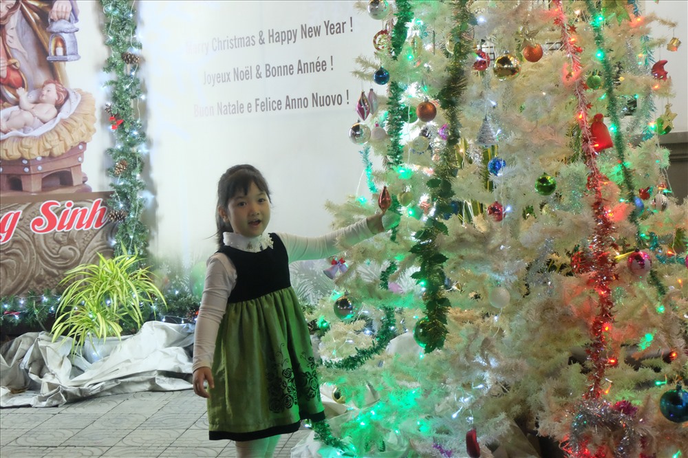Một em bé tạo dáng chụp ảnh bên cây thông Noel ở trong nhà thờ.
