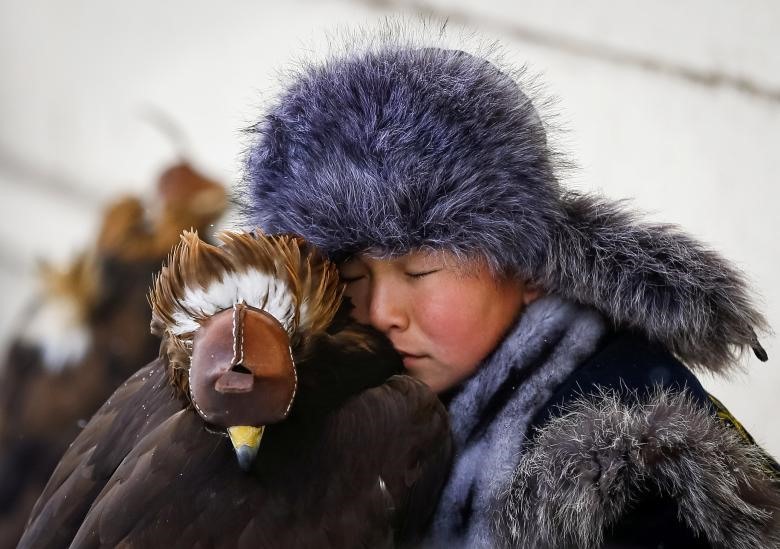 Một thợ săn trẻ đang nghỉ ngơi bên cạnh con đại bàng của mình trong cuộc thi đại bàng săn hàng năm ở Kazakhstan