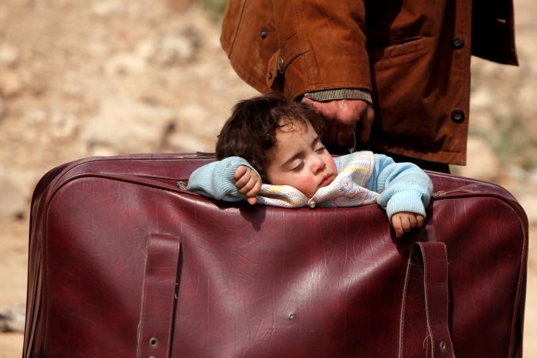 Một đứa trẻ ngủ ngon lành trong một cái túi ở làng Beit Sawa, phía đông Ghouta, Syria, khi em theo gia đình bắt đầu cuộc hành trình di cư không rõ ngày mai sẽ ra sao.