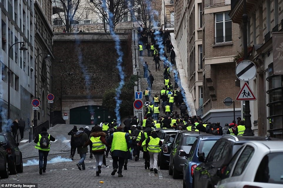 Người biểu tình đi lên cầu thang khi hơi cay được bắn gần khu vực Passy ở Paris khi những ngọn lửa màu xanh lam chảy xuống các bậc thang