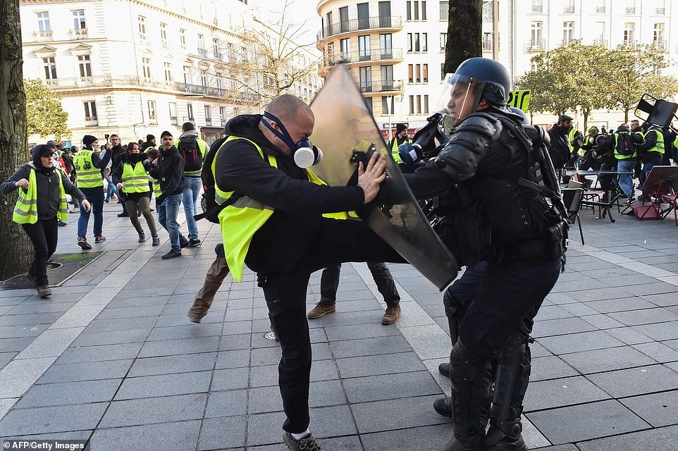 Một người biểu tình mặc vest vàng và đeo mặt nạ phòng độc cố gắng đá một sĩ quan cảnh sát chống bạo động Pháp trong một cuộc biểu tình chống lại chi phí sinh hoạt gia tăng, tại trung tâm thành phố Nantes, miền tây nước Pháp