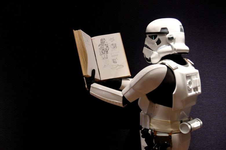 Một người đàn ông mặc trang phục Stormtrooper cầm quyển sổ phác thảo của nhà thiết kế trang phục John Mollo, hiển thị hình minh họa cho trang phục Chiến tranh giữa các vì sao, trong một cuốn sách quảng cáo trước buổi đấu giá tại Bonhams ở trung tâm London, ngày 6.12. Ảnh: REUTERS.