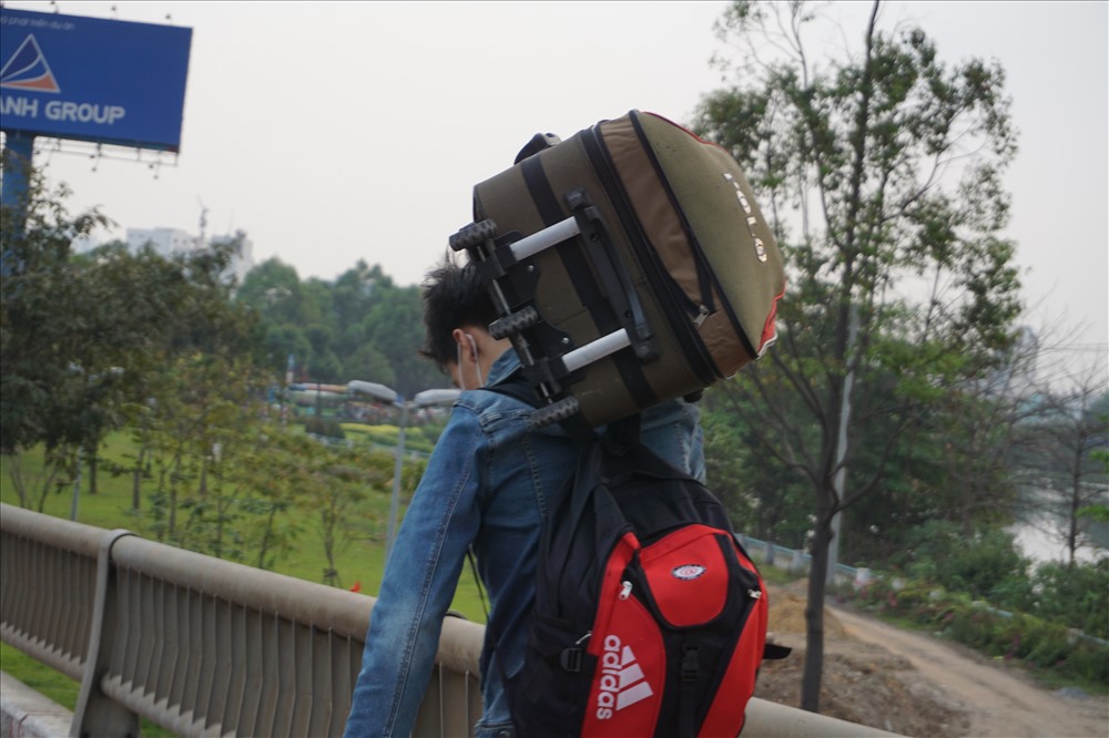Thanh niên còng lưng vác vali đi bộ trên cầu Bình Triệu