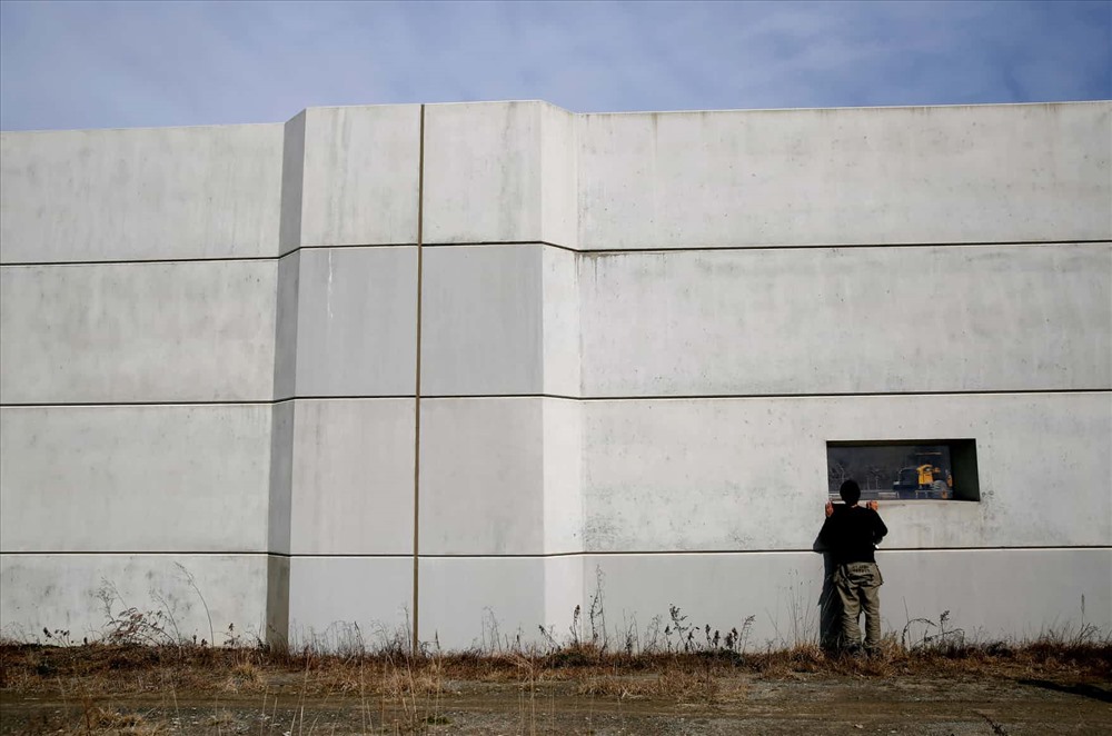 Một người đàn ông nhìn qua cửa sổ của bức tường biển ở Kesennuma. Nhiều người dân ban đầu hoan nghênh ý tưởng xây tường biển, nhưng dần dần cảm thấy tù túng, nói rằng họ không được hỏi ý kiến đầy đủ trong quá trình lên kế hoạch xây tường. Ảnh: Reuters