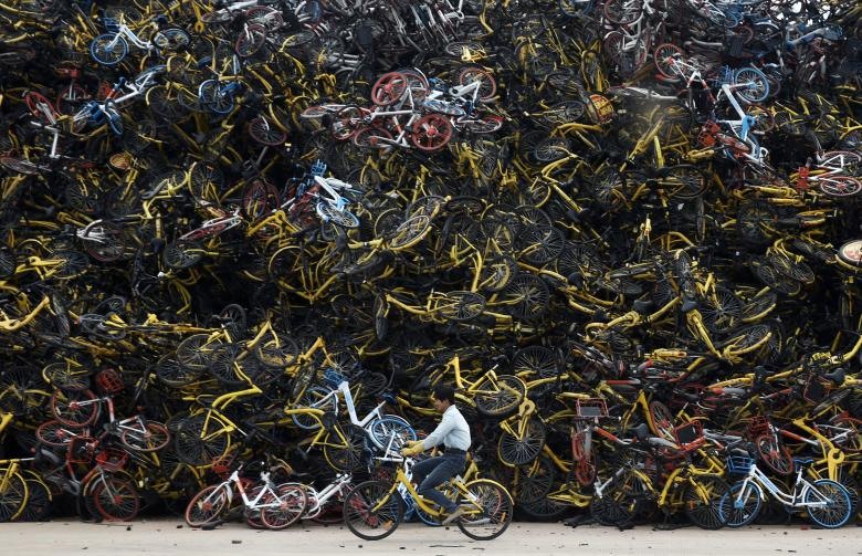 Một công nhân đang lái chiếc xe đạp đã qua sử dụng giữa hàng nghìn chiếc xe đạp chia sẻ nằm chất chồng lên nhau tại một khu đất ở Hạ Môn, tỉnh Phúc Kiến. (Ảnh: REUTERS)