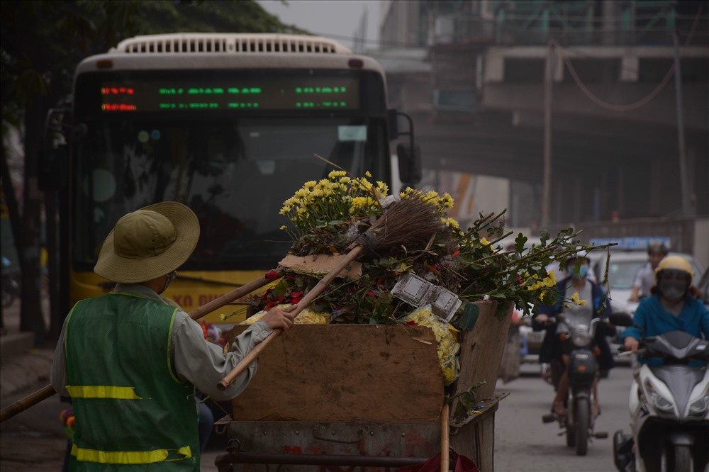 Người lao công thu gom những bó hoa bị bỏ lại bên những sạp bán hoa ven đường.