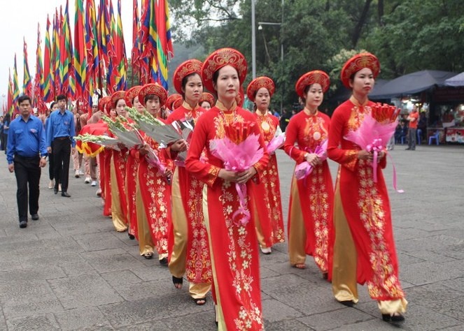 Nhiều cô gái mặc áo dài mang theo lễ vật và gần 100 chàng trai Đất Tổ cầm  cờ lễ tiến về phía đền Thượng dâng hương.
