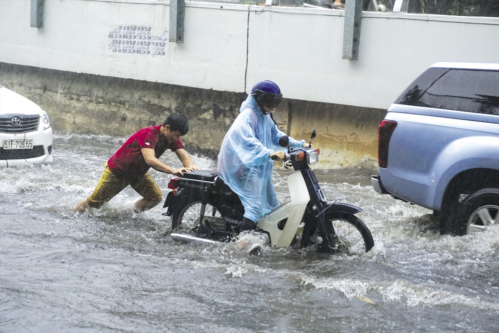 Hì hục đẩy xe chết máy qua đường ngập Nguyễn Hữu Cảnh trong cơn mưa chiều 7.5. Ảnh: Minh Quân