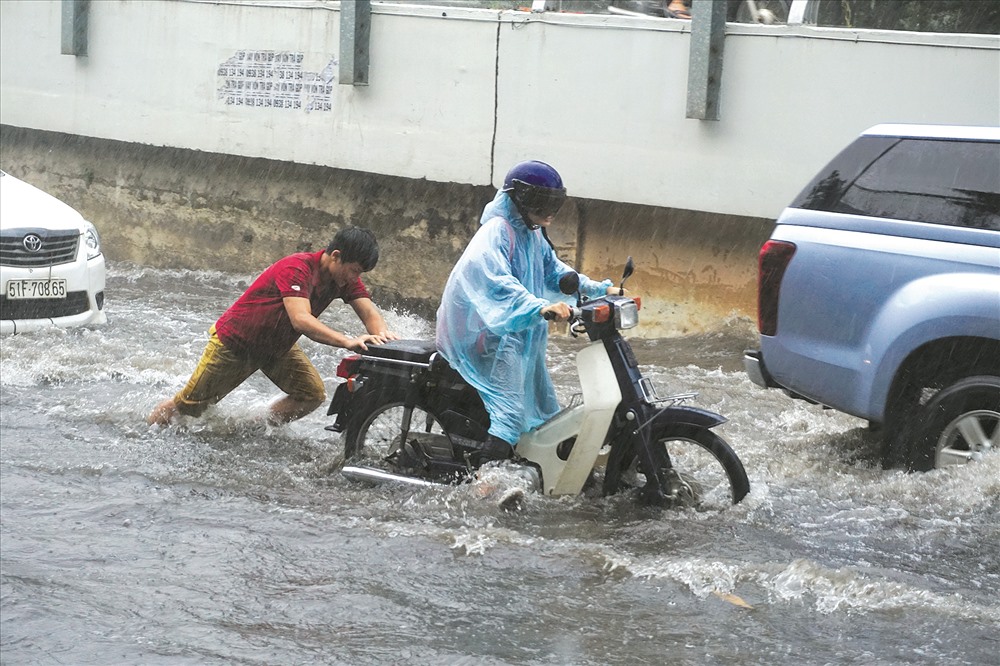 Hì hục đẩy xe chết máy qua đường ngập Nguyễn Hữu Cảnh trong cơn mưa chiều 7.5. Ảnh: Minh Quân