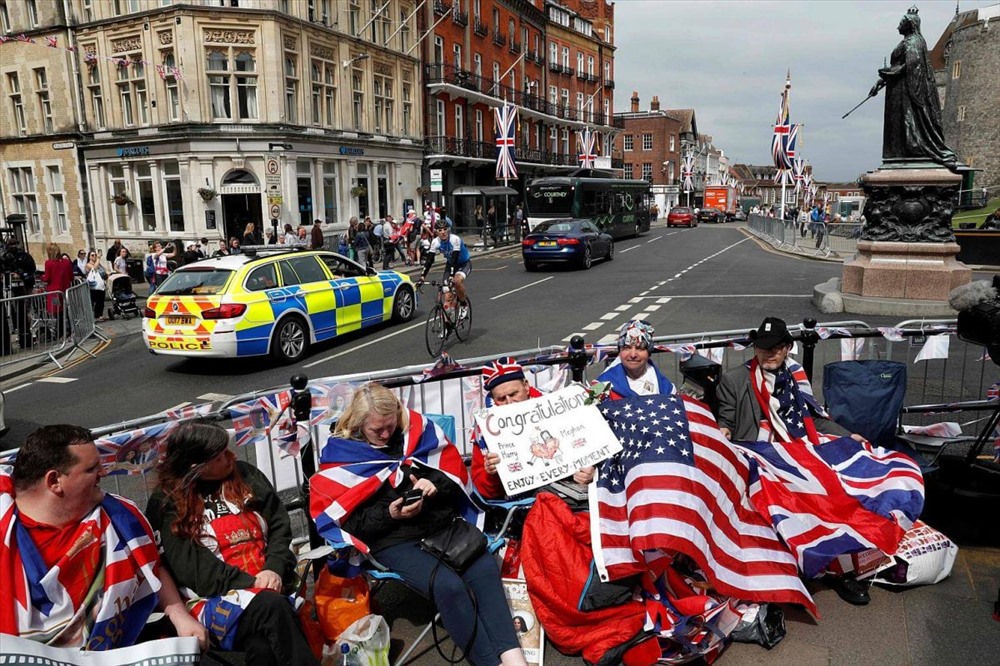 Người hâm mộ mang theo cờ Anh và cờ Mỹ, ngồi ở góc phố dọc theo tuyến đường lễ rước trong hôn lễ hoàng gia Anh đi qua để giữ chỗ. Ảnh: AFP
