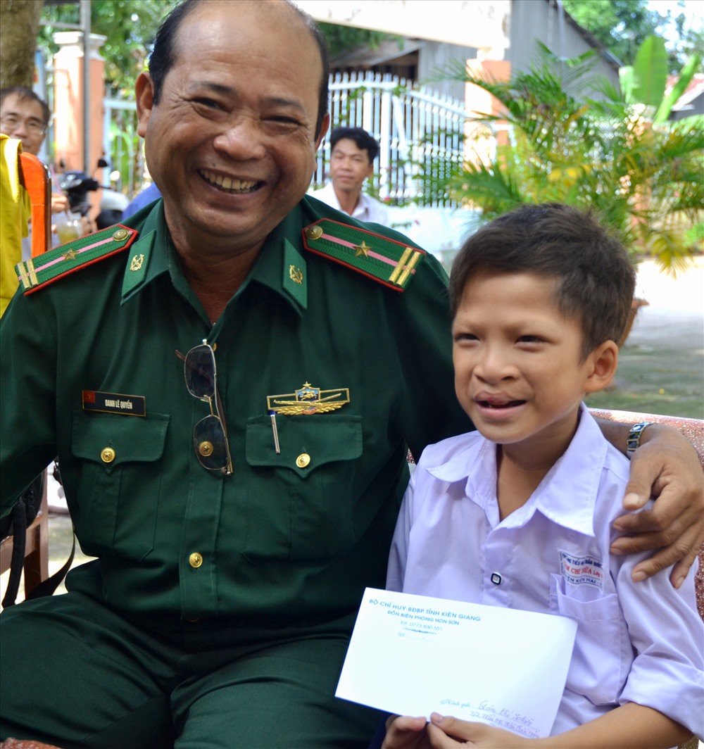 Thiếu tá Danh Lê Quyền trao tiền hỗ trợ cho học sinh Lâm Chí Thừa (SN 2009, ấp Bãi Nhà A, xã Lại Sơn) bị dị tật bẩm sinh, mồ côi cha, sống với nội. (Ảnh: Lục Tùng)