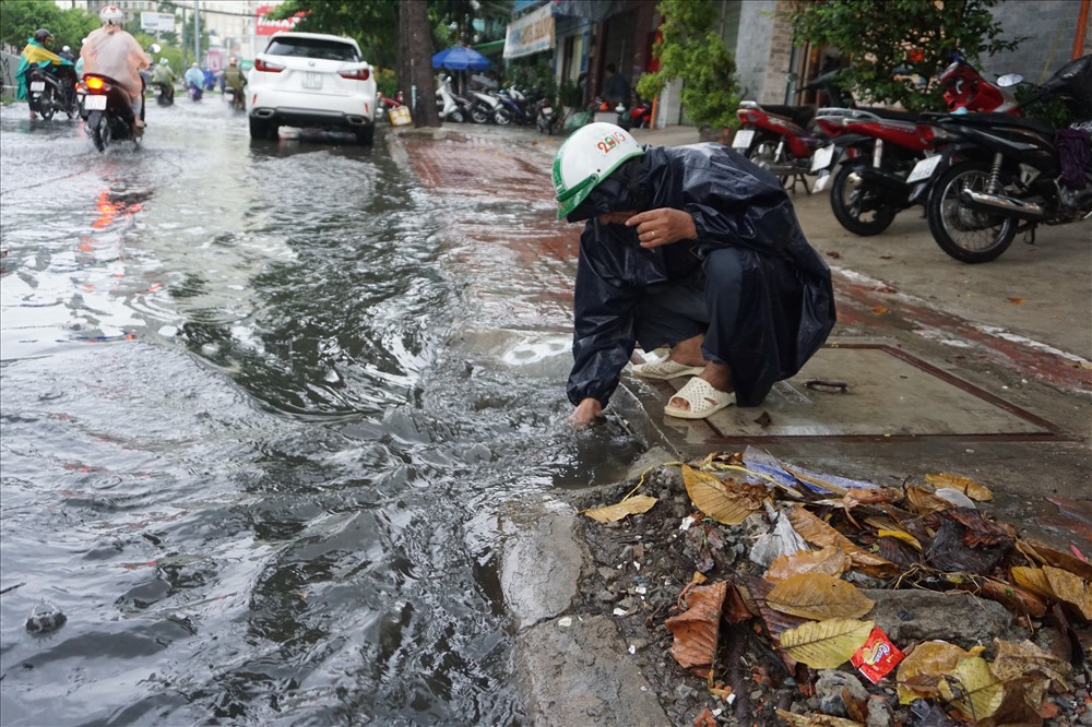 Công nhân Cty thoát nước đô thị thành phố thò tay móc rác từ trong miệng cống trên đường Nguyễn Hữu Cảnh.
