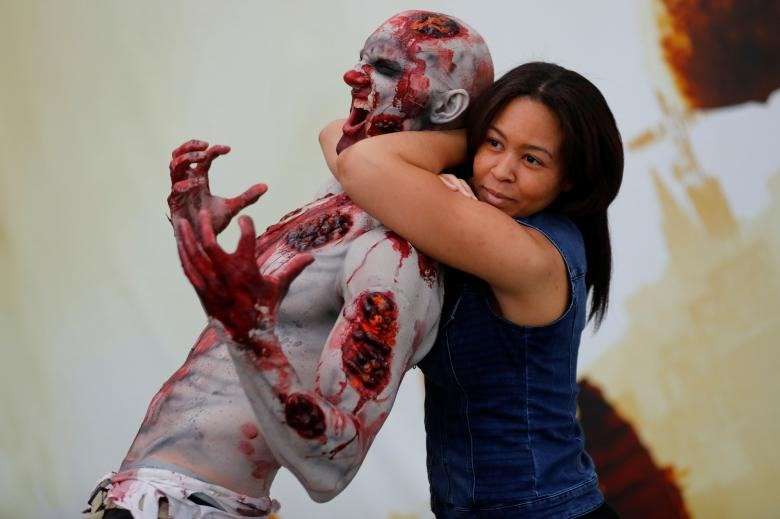Một người tham dự hội chợ E3 chụp ảnh với một zombie.  E3 là viết tắt của Electronic Entertainment Expo, đây là một hội chợ giới thiệu sản phẩm của các hãng game trong nền công nghiệp game. Đây là một sự kiện độc quyền, được tổ chức bởi Hiệp hội phần mềm giải trí (Entertainment Software Association – ESA). Ảnh:  Mike Blake / REUTERS.