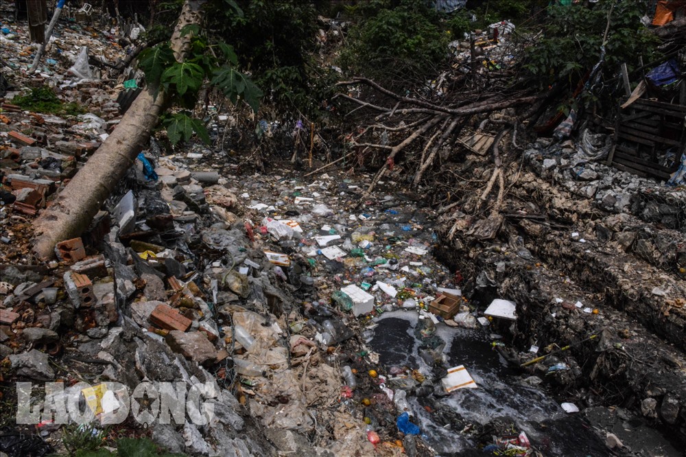 Phía dưới chân cầu Long Biên, nhiều loại rác thải vứt ngổn ngang, dòng nước đen ngàu, đặc kịt.