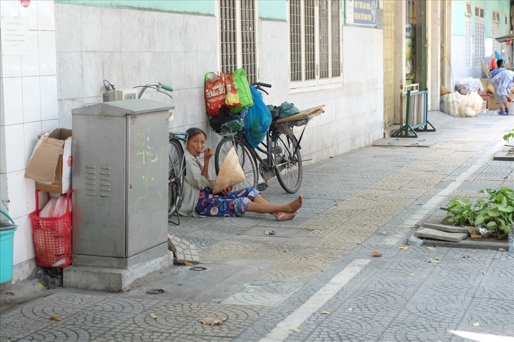 Một người phụ nữ buôn ve chai tranh thủ ngồi nghỉ trên vỉa hè để lấy sức