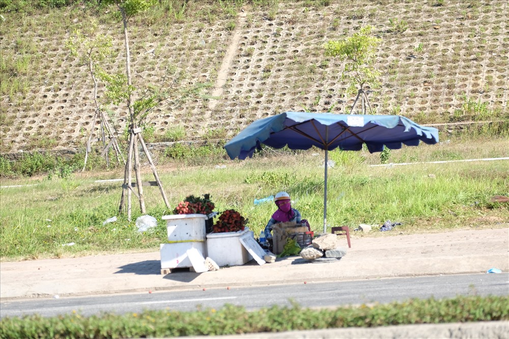 Một người phụ nữ che dù ngồi bán trái cây ven đường giữa trời nắng nóng