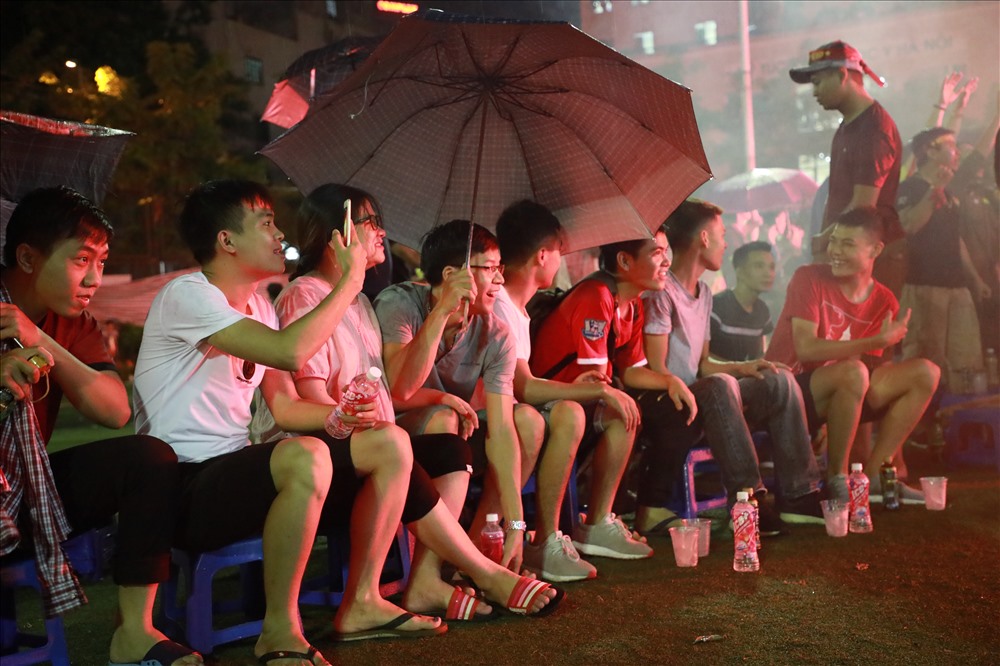 Các cổ động viên mặc áo mưa, che ô vẫn chăm chú theo dõi diễn biến trận bóng.