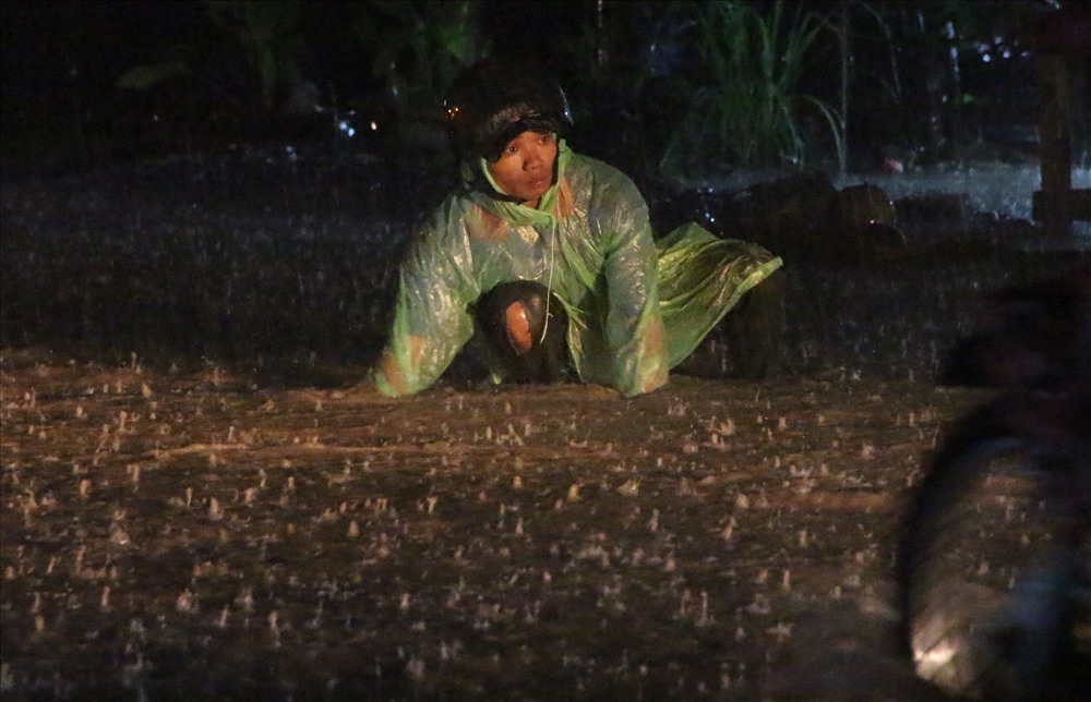 Một công nhân phải dầm mình dưới mưa mò lại đồ bị rơi.