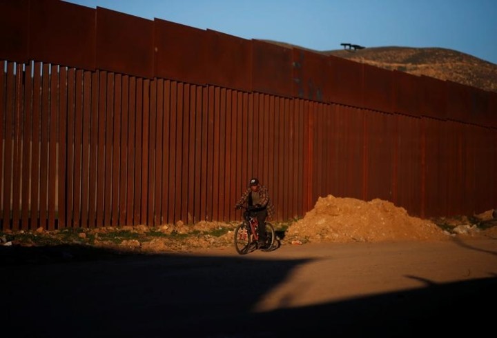 Một người đàn ông đi xe đạp gần biên giới phân chia Hạt San Diego California, Mỹ và Tijuana.