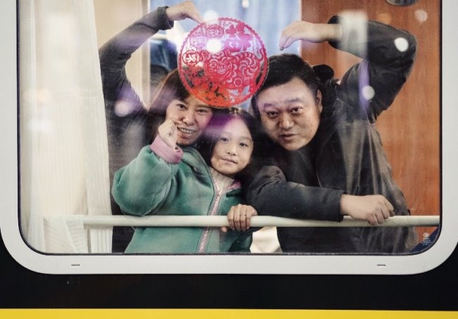 Một cô gái và cha mẹ cô chụp một bức ảnh đằng sau cửa sổ “Nhân vật may mắn” trên một chuyến tàu tại Ga xe lửa Bắc Kinh. Ảnh: China Plus