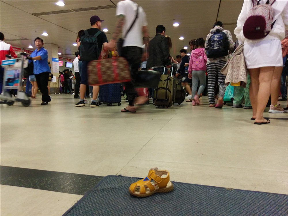 Một chiếc giầy của trẻ nhỏ bị rơi tại sân bay, nhiều người hối hả bước qua làm thủ tục cho kịp giờ bay.