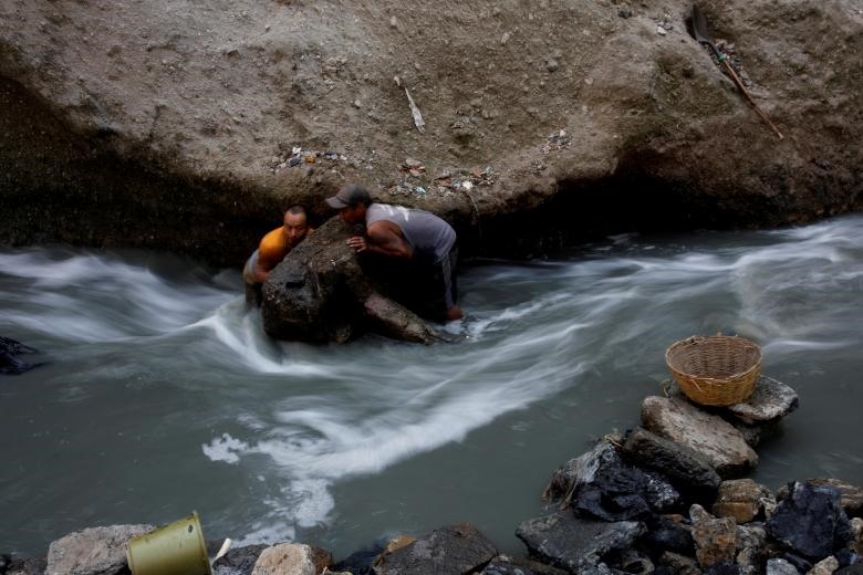 Nhiều người dân nghèo đã đổ xô đến Mine - bãi rác lớn nhất thành phố Guatemala để tìm kiếm những mảnh kim loại phế liệu. Dường như bãi rác này đã trở thành nơi mưu sinh của họ. Trong hình là hai người đàn ông di chuyển một tảng đá trong dòng nước thải ô nhiễm tại “vựa rác thải” lớn nhất thành phố Guatemala. Ảnh: Reuters.