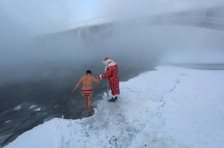 Một người đàn ông hóa trang thành Ded Moroz (ông già Noel của Nga) để giúp một thành viên của câu lạc bộ bơi lội mùa đông nghiệp dư Cryophile, đi bộ vào vùng nước băng giá của sông Yenisei để đánh dấu năm mới và mùa Giáng sinh. Nhiệt độ ngoài trời khoảng âm 26 độ C, ở Krasnoyarsk, Nga. Ảnh: Reuters.