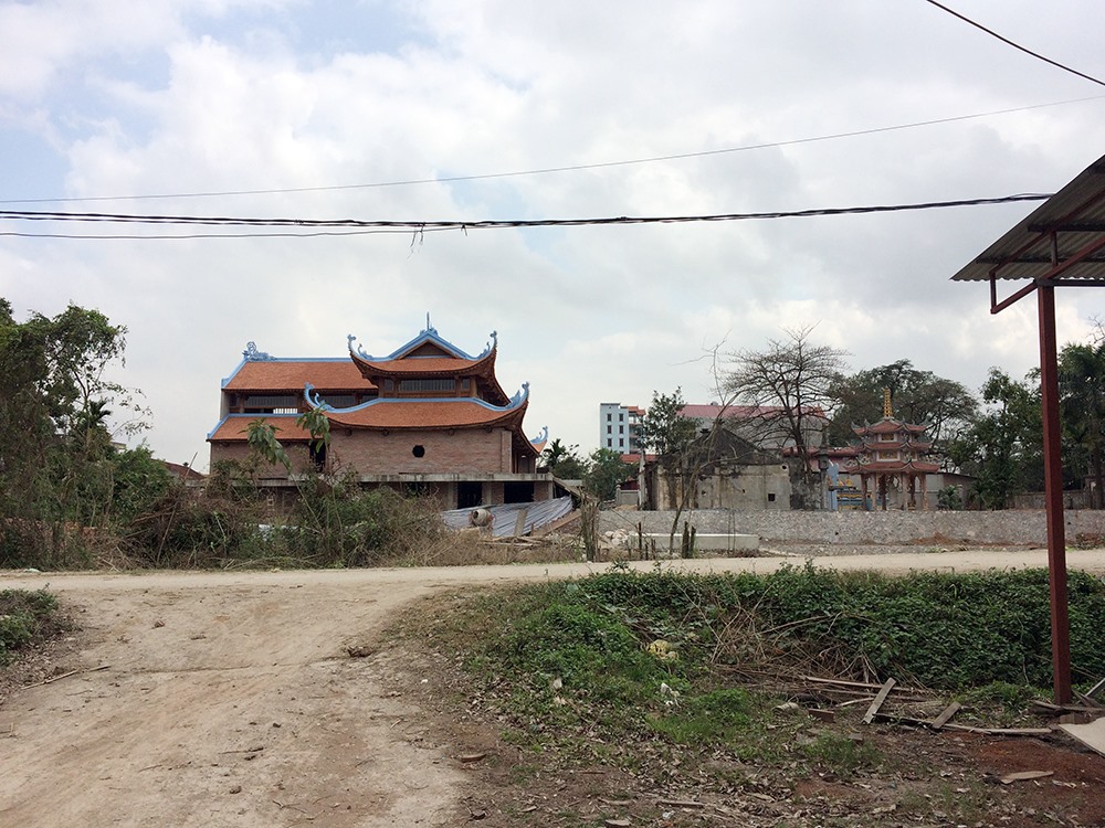 Phía bên kia con đường là ngôi chùa cũ nằm thọt lỏm cạnh ngôi chùa mới bề thế đang trong giai đoạn thi công.