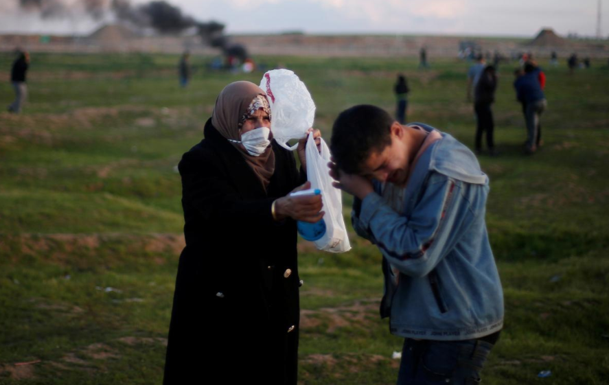 Một người phụ nữ giúp một cậu bé Palestine sau khi hít phải hơi cay bắn ra bởi quân đội Israel / Ảnh: Reuters