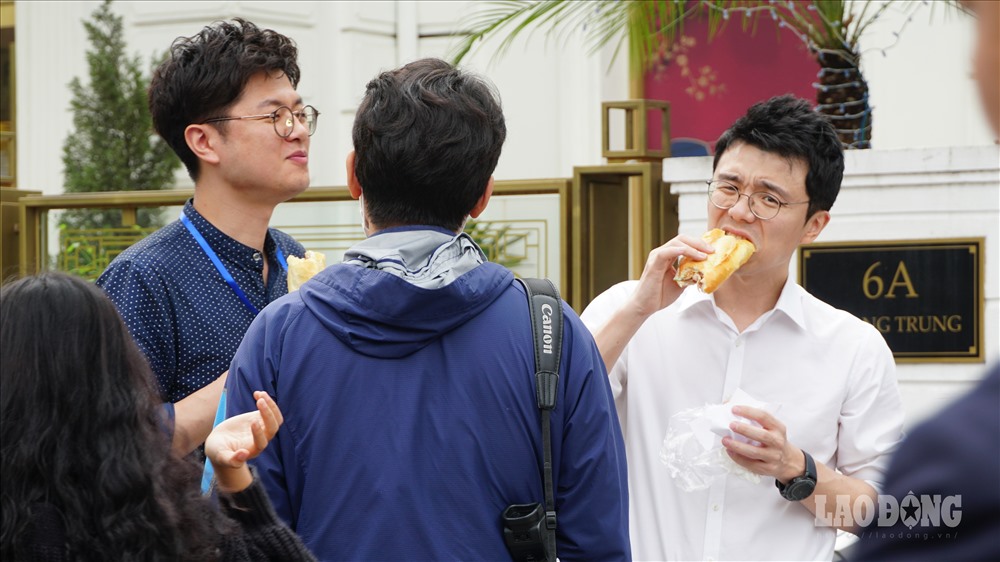 Một số phóng viên khác của Hàn Quốc vừa trò chuyện, vừa ăn vội bánh mỳ - một món ăn đường phố nổi tiếng ở Việt Nam. 