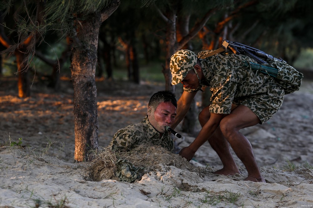 Ẩn mình dưới cát liên tục hàng giờ đồng hồ là một trong những kỹ năng được các chiến sĩ đặc công nước đặc biệt chú trọng luyện tập. Trong ảnh, một chiến sĩ đặc công nước được đồng đội hỗ trợ sau khi thực hiện nội dung nguỵ trang dưới cát.