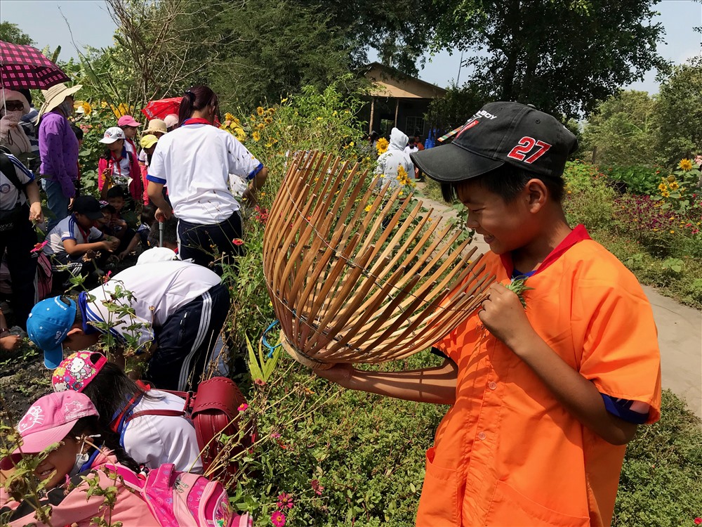 Một cậu bé thích thú với chiếc nôm cá, chuẩn bị trải nghiệm hoạt động “1 giờ làm nông dân” tại cánh đồng hoa Vĩnh Hiệp