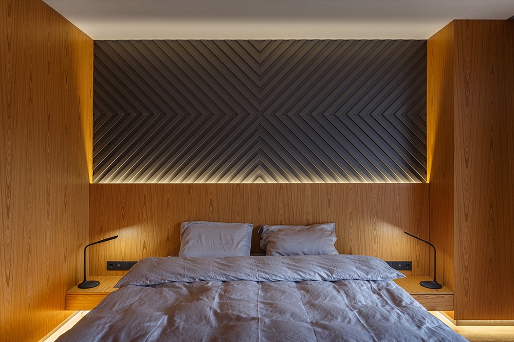 Trang trí phòng ngủ hiện đại kết hợp một bức tường đặc trưng kết cấu, được nhấn mạnh bởi ánh sáng phía sau đầu giường. Hai đèn bàn cạnh giường ngủ cung cấp ánh sáng nhiệm vụ.