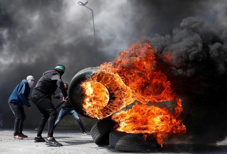 Một người biểu tình Palestine di chuyển một chiếc lốp xe đang cháy trong cuộc đụng độ với quân đội Israel gần khu định cư của người Do Thái Beit El, ở Bờ Tây do Israel chiếm đóng. Ảnh: Reuters.