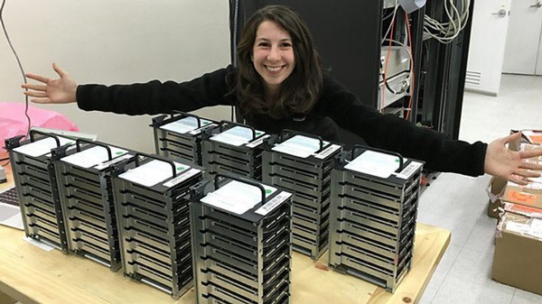 Katie cười tươi bên cạnh chồng ổ cứng máy tính lưu trữ dữ liệu nghiên cứu hố đen vũ trụ.