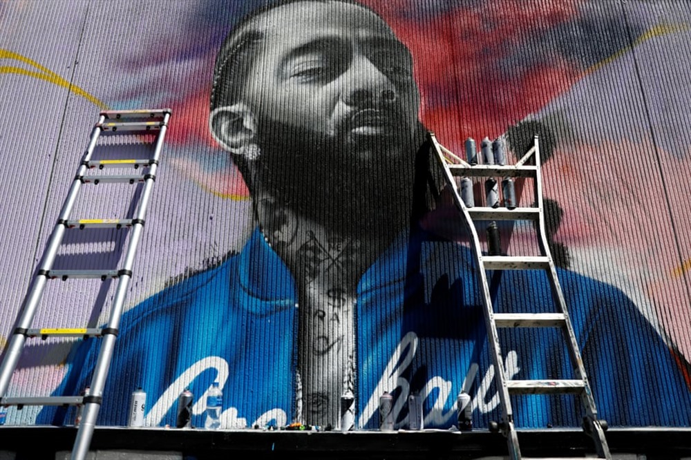 Một nghệ sĩ làm việc trên một bức tranh tường của rapper bị giết, đồng thời là nhà từ thiện Nipsey Hussle bên ngoài cửa hàng quần áo thể thao của nhạc sĩ ở California (Ảnh: Patrick T Fallon / Reuters tại Los Angeles - Mỹ)