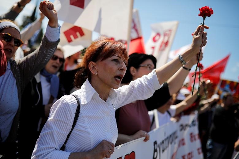 Những người biểu tình cầm hoa cẩm chướng và hát vang bài hát quốc tế ca trong cuộc mít tinh diễn ra tại Athens, Hy Lạp.