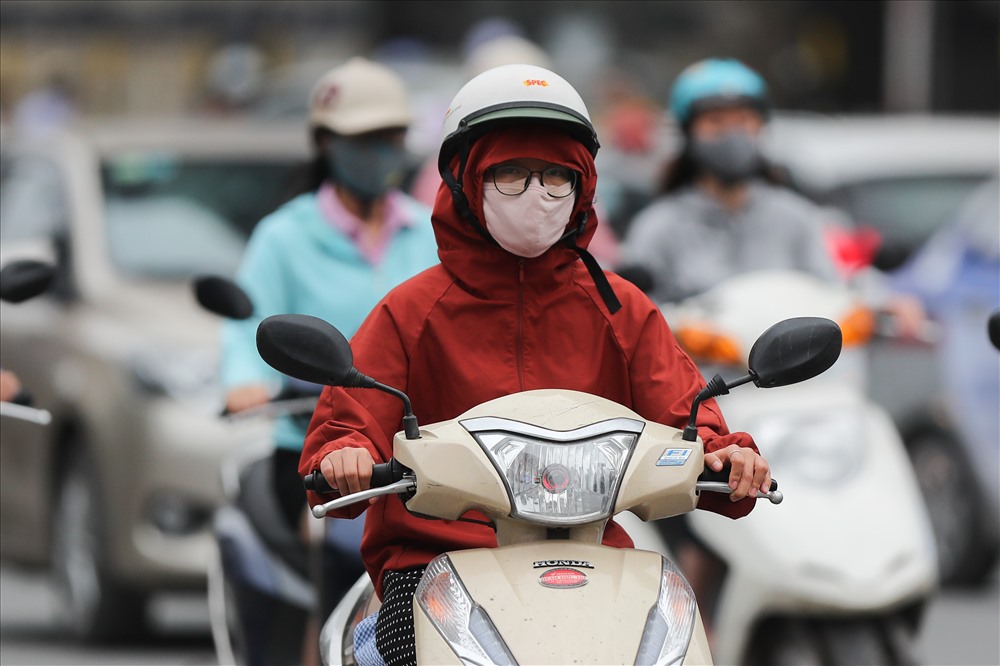 Người phụ nữ mặc áo khoác kín, đội mũ kín đầu chạy xe máy giữa thời tiết tháng 5.