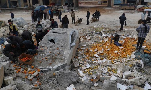 Người dân nhặt những quả cam giữa đống đổ nát sau cuộc không kích của phiến quân vào khu chợ ở tỉnh Idlib (Syria) ngày 14.1.2017. Ảnh: TL