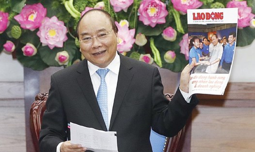 Thủ tướng Nguyễn Xuân Phúc giơ cao ấn phẩm đặc biệt của báo Lao Động “Báo chí đồng hành cùng người lao động và doanh nghiệp” tại cuộc họp của Chính phủ nhân 21.6.2017.