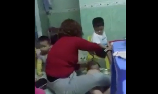 Hình ảnh bảo mẫu nhóm trẻ Mẹ Mười đè một em nhỏ ra đổ thức ăn vào miệng. Ảnh cắt từ clip