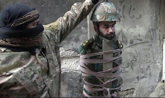 Tay súng IS đặt mũ chứa đầy thuốc nổ vào đầu binh sĩ Syria. Ảnh: Mirror