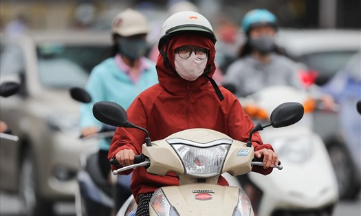 Người phụ nữ mặc áo khoác kín, đội mũ kín đầu chạy xe máy giữa thời tiết tháng 5.