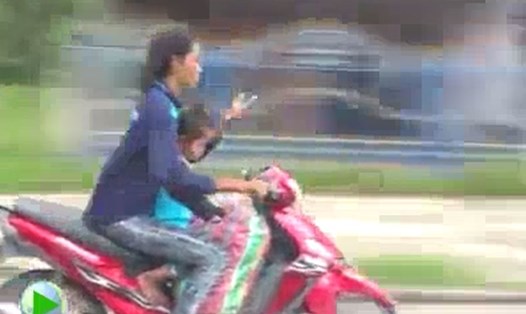 Hình ảnh người phụ nữ chở con nhỏ, không đội mũ bảo hiểm, buông 2 tay, lướt điện thoại. Ảnh cắt từ clip