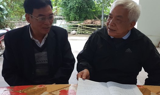 Ông Lê Nguyên Tố (phải) và ông Nguyễn Duy Lộc (trái) lần dở từng trang ghi chép cẩn thận về các câu chuyện lịch sử tại xã. Ảnh: HN